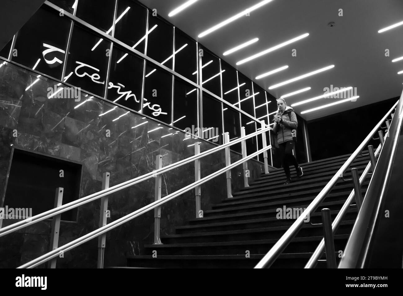 Belgrado, Serbia - 20 novembre 2023: Ragazza adolescente che scende le scale della metropolitana, con luci interne riflettenti e insegna dei grandi magazzini di Belgrado Foto Stock