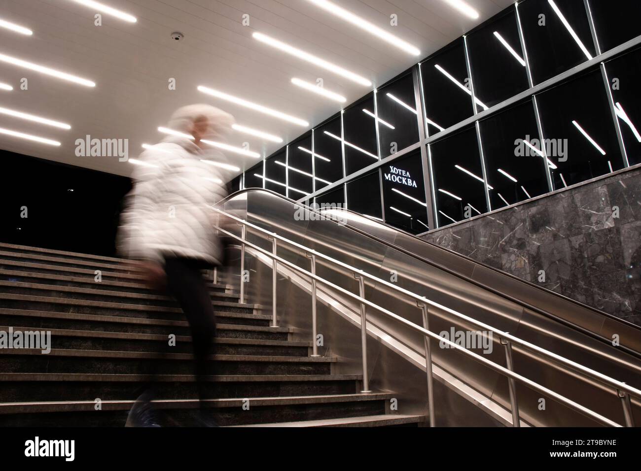 Belgrado, Serbia - 20 novembre 2023: Persona sfocata che scende le scale della metropolitana con riflessi di luci interne e insegna dell'hotel Mosca in cirillico Foto Stock