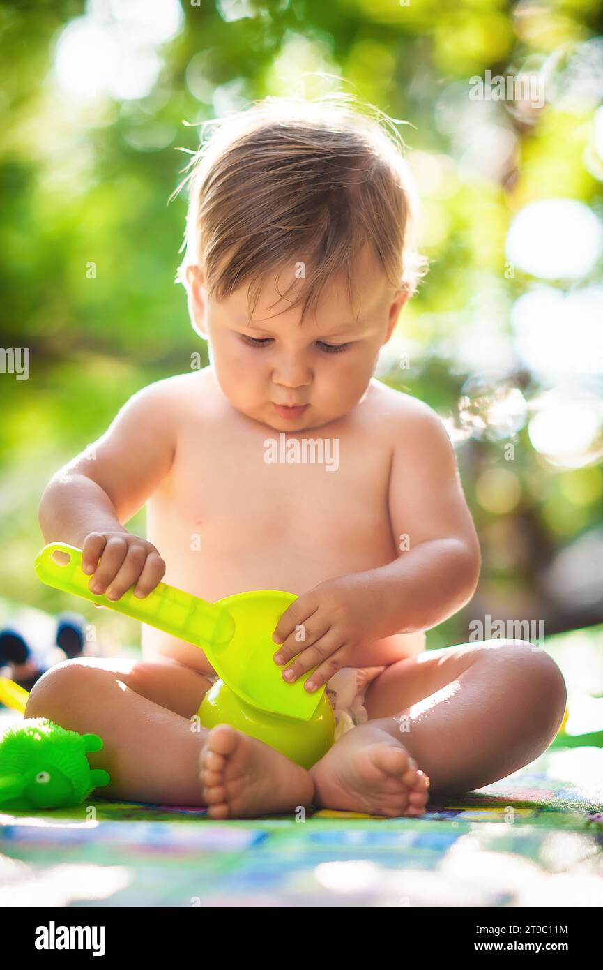 Bambino seduto in giardino e che gioca con i giochi d'acqua. Calda giornata estiva nella natura Foto Stock