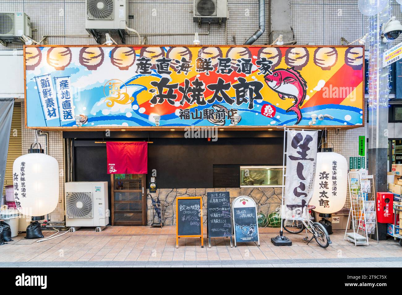 Ristorante izakaya giapponese di stile moderno. Grande cartello con i nomi sopra l'entrata, varie tavole del menu all'esterno con grande chochin bianco e lanterna. Foto Stock