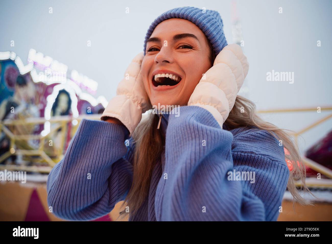 Una donna allegra ed elegante, vestita con abiti caldi, si diverte in un parco divertimenti invernale innevato. Foto Stock