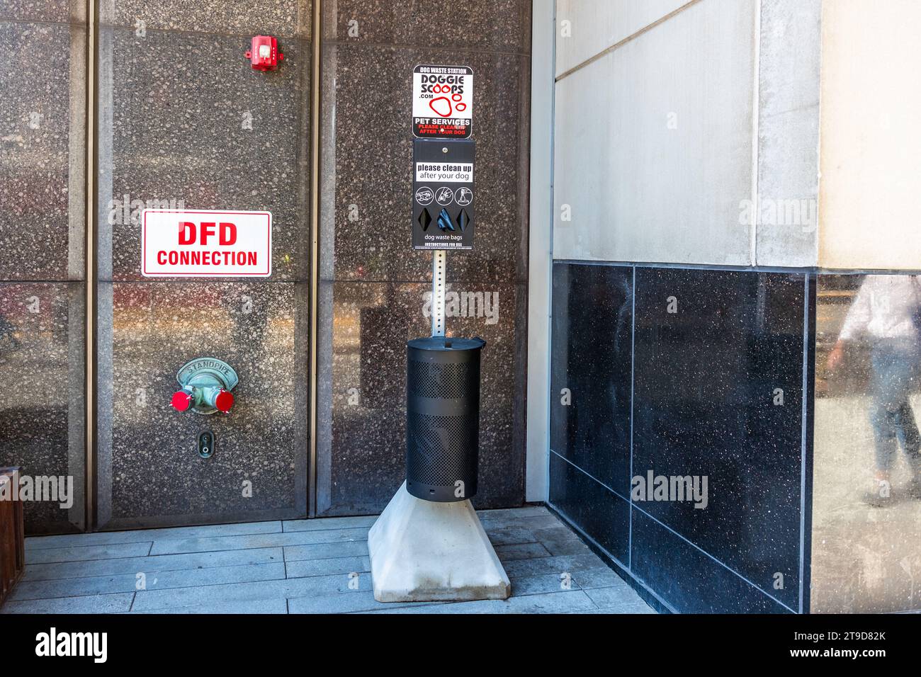 Una stazione per sacchetti per deiezioni canine della marca "Doggie Scoops" si trova accanto a un raccordo per idrante del Dipartimento dei Vigili del Fuoco di Detroit ("DFD Connection") davanti a una facciata in pietra lucida nel centro di Detroit, Michigan, Stati Uniti. Un cartello chiede ai proprietari di cani di pulire dietro i loro animali domestici. Foto Stock