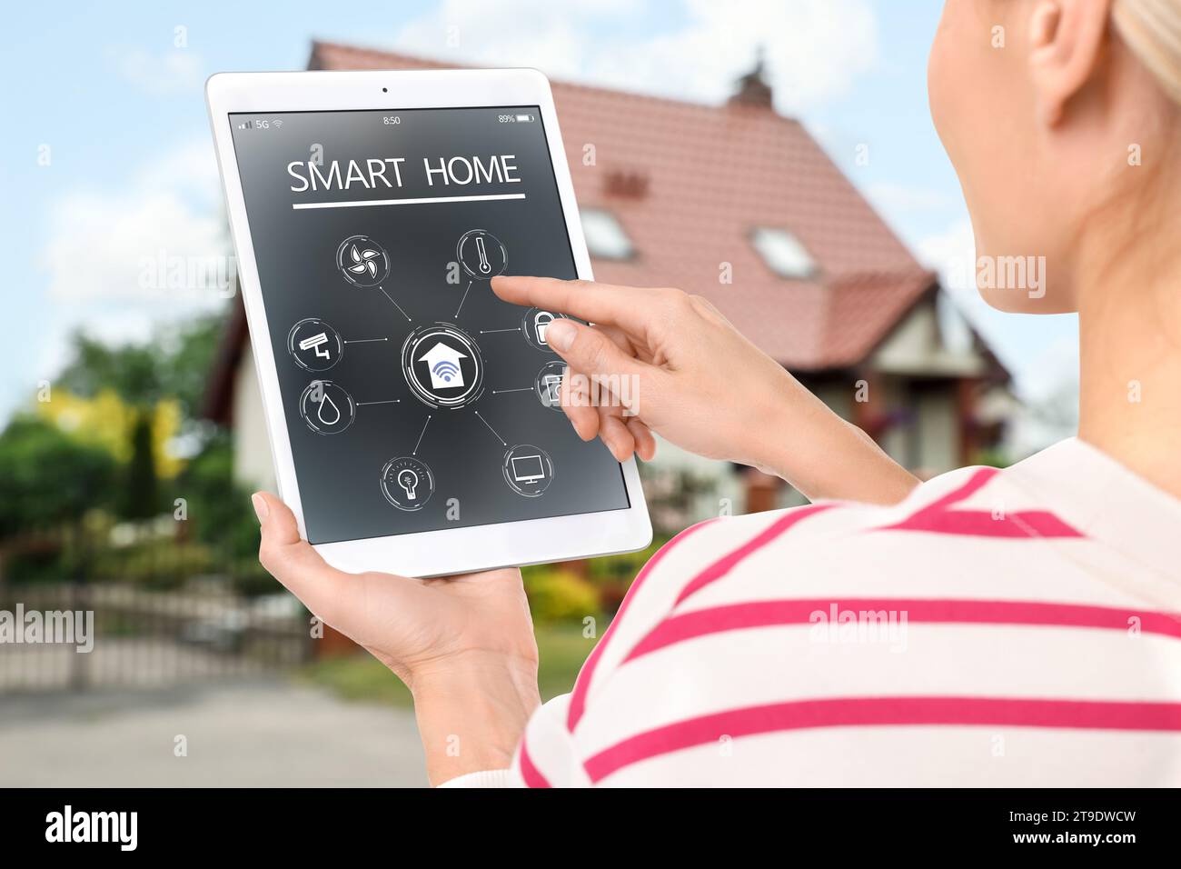 Donna che utilizza un sistema di controllo domestico intelligente tramite tablet vicino a casa all'aperto, primo piano Foto Stock