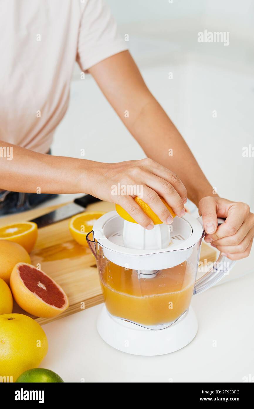 Primo piano della centrifuga per agrumi e mani femminili durante la preparazione del succo d'arancia fresco Foto Stock