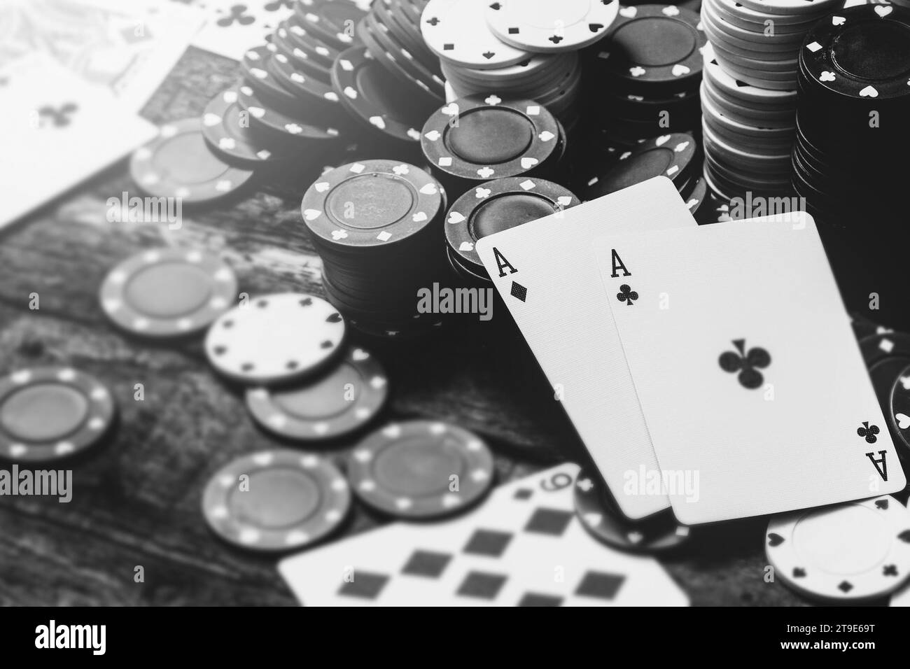 Immagine monocromatica di due assi e un sacco di chip da casinò su un tavolo di legno Foto Stock