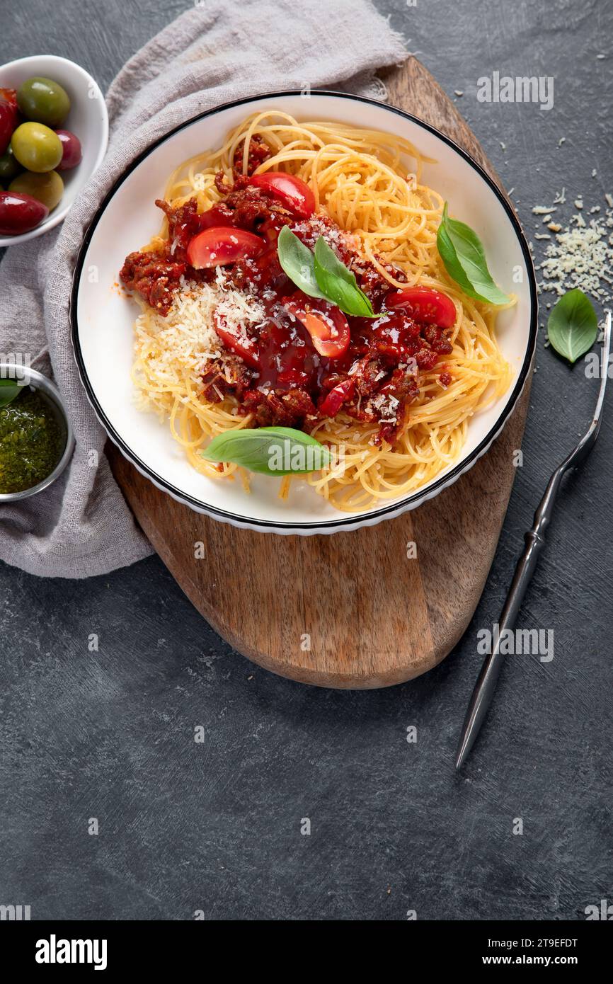 Gustosi e appetitosi spaghetti italiani classici, pasta alla bolognese con salsa di pomodoro, parmigiano di formaggio, carne e basilico su piatto su sfondo scuro. Vista dall'alto. Foto Stock