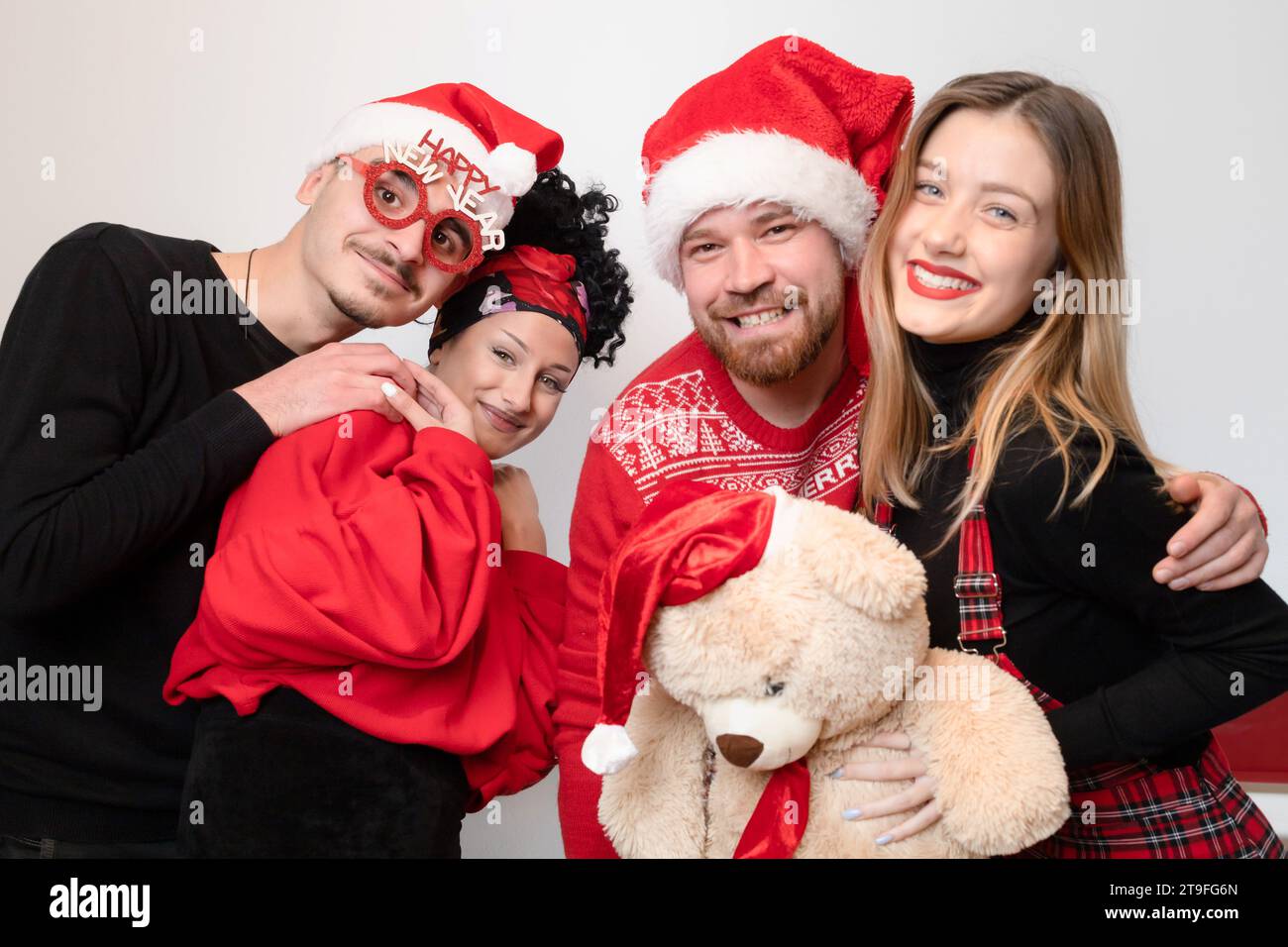 Quattro amici che festeggiano il nuovo anno, con un aspetto felice e allegro con occhiali prop e orsacchiotto Foto Stock