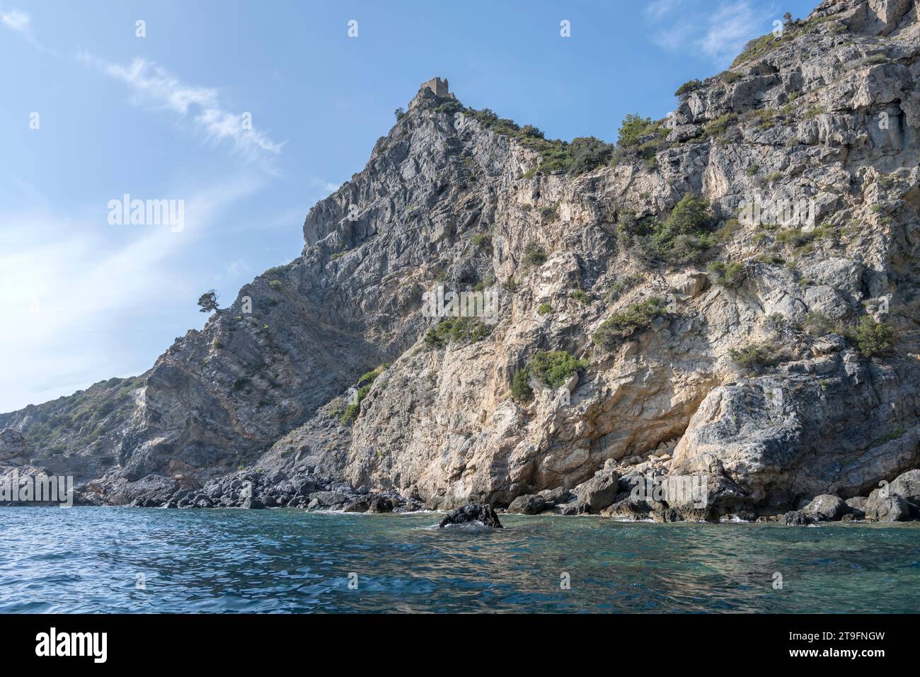 Paesaggio con ripide scogliere rocciose di capo Maddalena e vecchia torre in rovina sul promontorio sulla riva mediterranea, scattata da una barca in luminoso inizio autunno Foto Stock Paesaggio con ripide scogliere rocciose di capo Maddalena e vecchia torre in rovina sul promontorio sulla riva mediterranea, scattata da una barca in luminoso inizio autunno Foto Stock