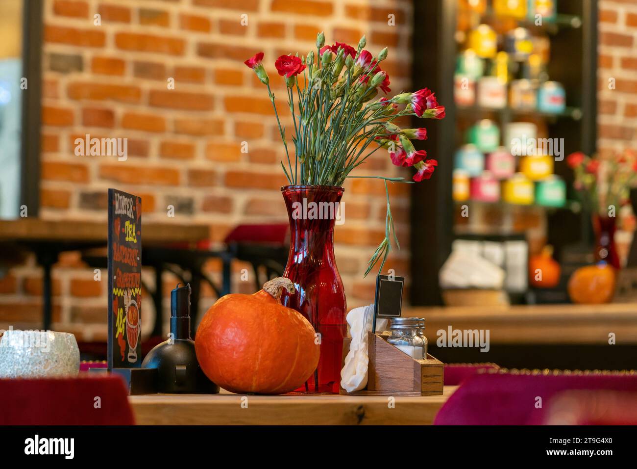 Interni rustici del ristorante con decorazioni autunnali con luce ambiente, pareti in mattoni rossi e tavolo in legno, eleganti e caldi arredi tranquilli Foto Stock