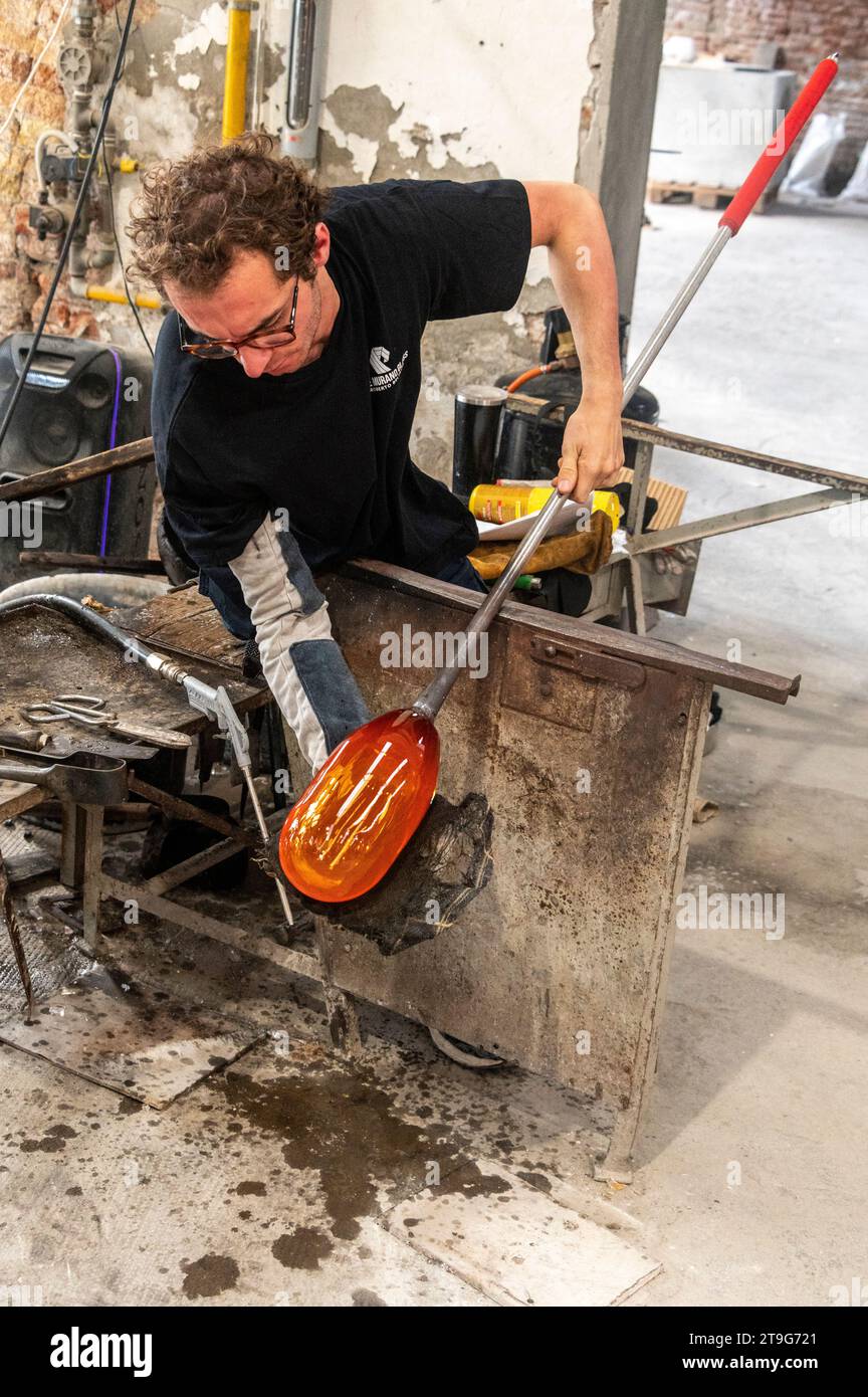 Un soffiatore di vetro forma abilmente uno stampo fuso riscaldato di vetro trasparente in un vaso di fiori artigianale presso il forno in vetro di Murano Wave, sull'isola di Foto Stock