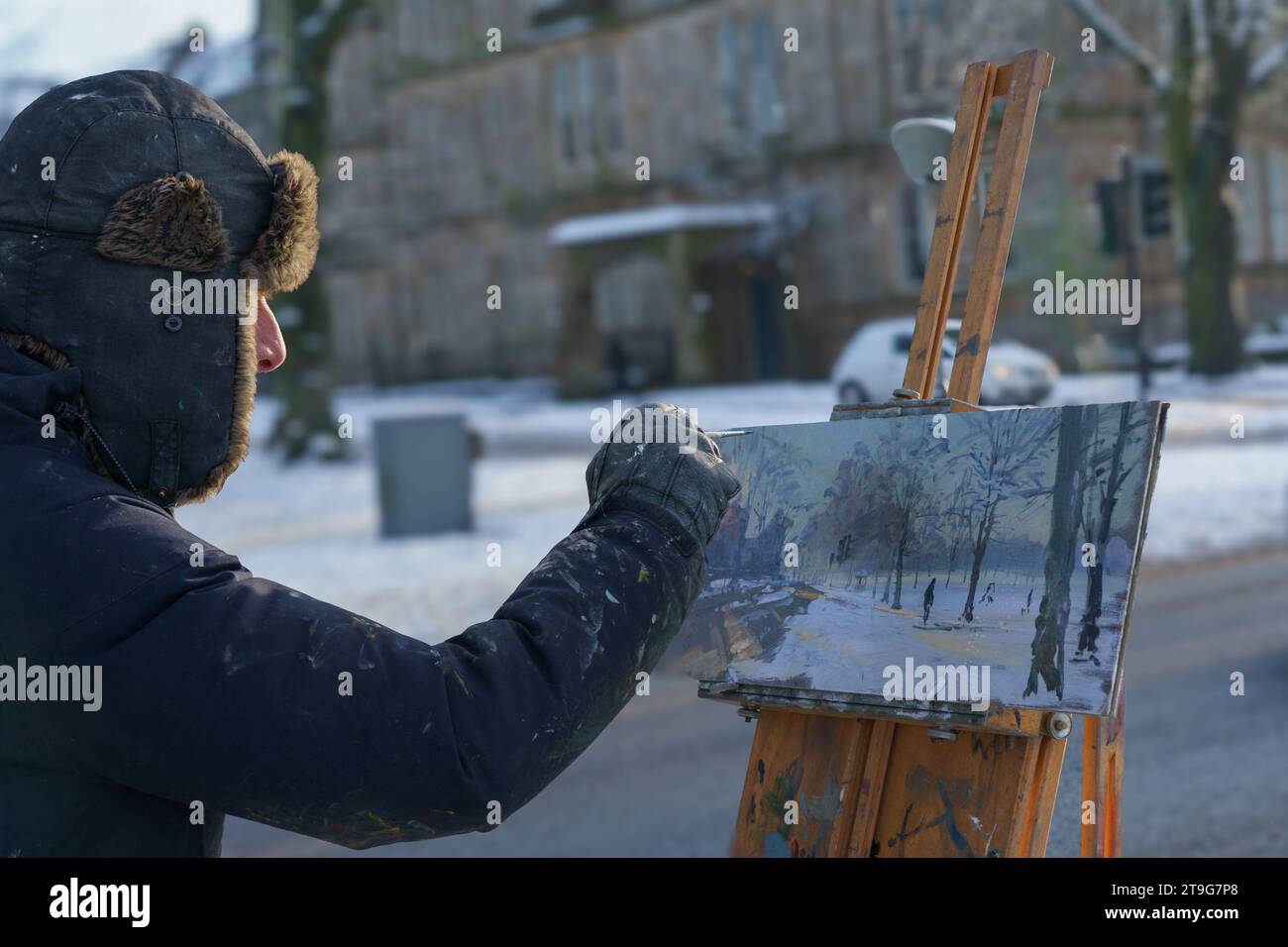 Un artista che utilizza un cavalletto di legno per sostenere una tela mentre dipinge una scena di un paesaggio invernale urbano, Harrogate, Yorkshire, Regno Unito. Foto Stock