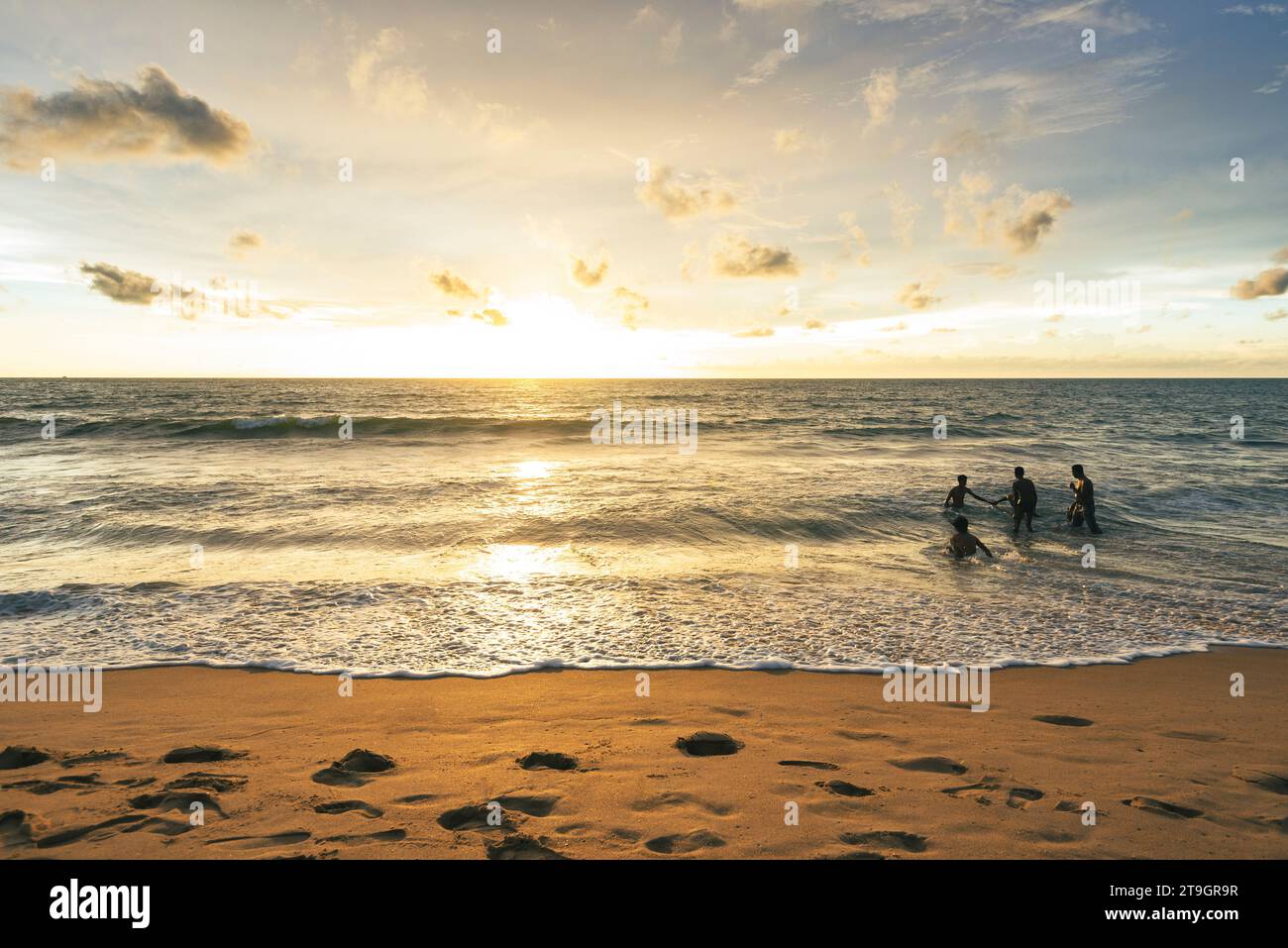 Un gruppo di amici si divertirà un po' di tempo in mare mentre il sole tramonta a Negombo, in Sri Lanka Foto Stock