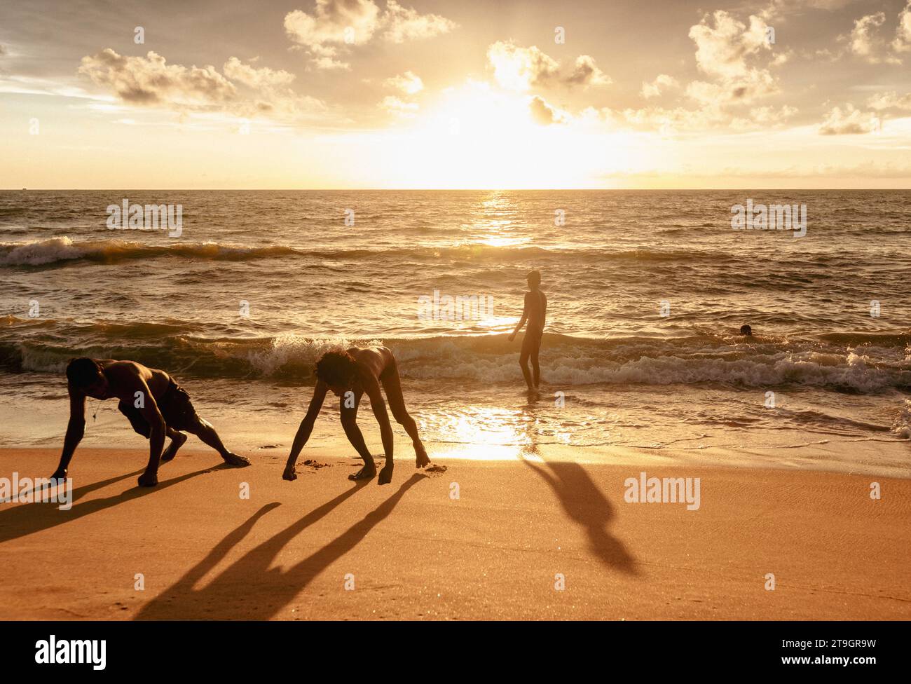 Due uomini locali si sfidano a vicenda per salire sulla spiaggia mentre il sole tramonta a Negombo, nello Sri Lanka Foto Stock