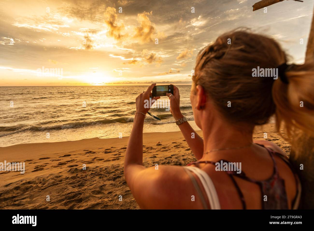 Una donna dai capelli biondi scatta una foto del tramonto all'orizzonte a Negombo, in Sri Lanka Foto Stock