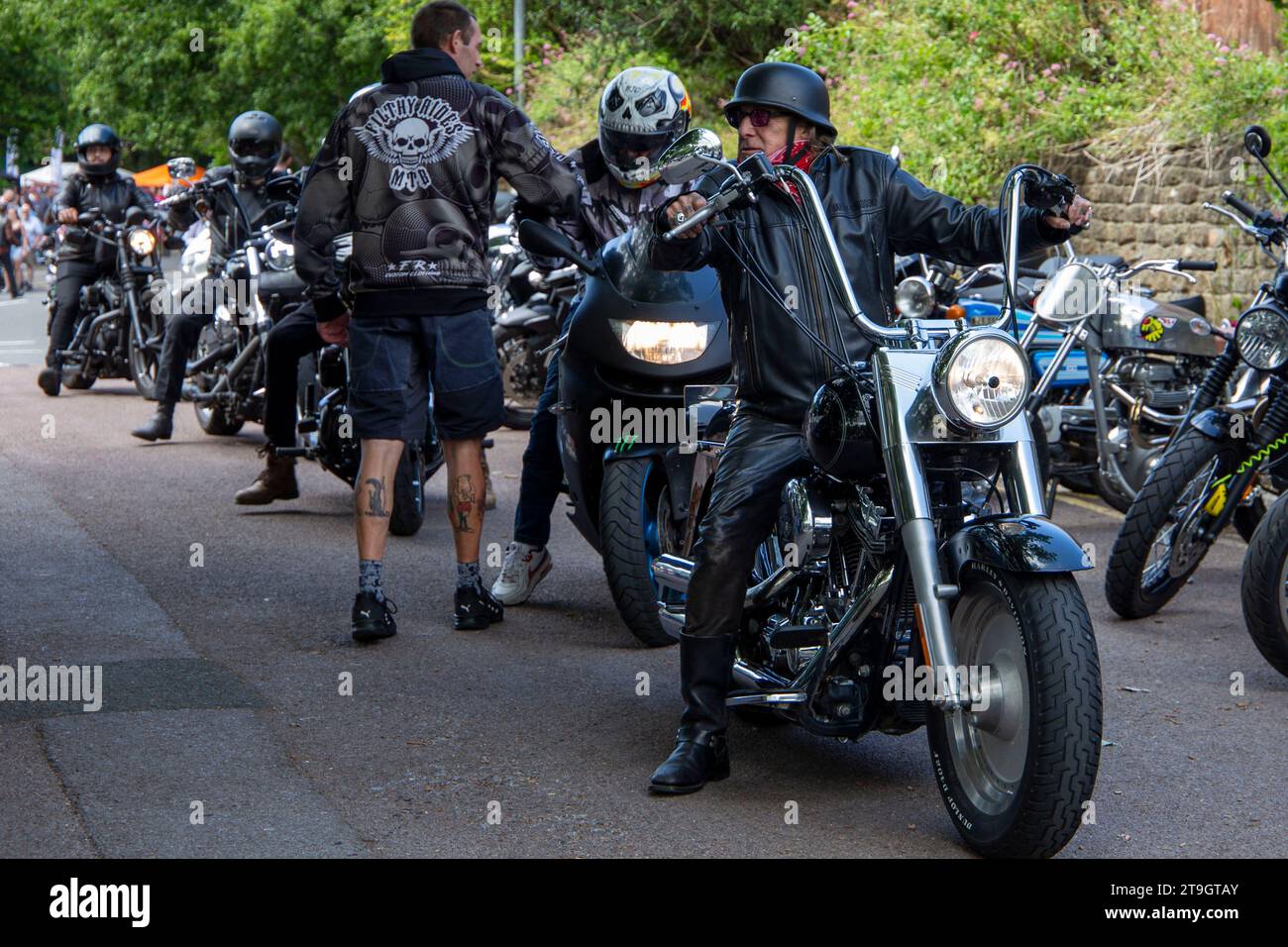 Motociclista in pelle su una moto Harley Davidson con manubrio della scimmia motociclista sullo sfondo con tatuaggi sulle gambe Calne Meet luglio 2023 Foto Stock