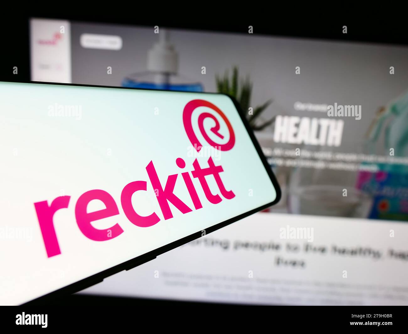 Telefono cellulare con logo della società di beni di consumo Reckitt Benckiser Group plc davanti al sito Web. Mettere a fuoco il display centrale destro del telefono. Foto Stock