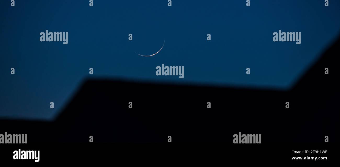 Una nuova luna a mezzaluna del 2% si staglia su una serie di tetti dal profilo unico, trasformando il familiare in un inafferrabile e irriconoscibile. Foto Stock