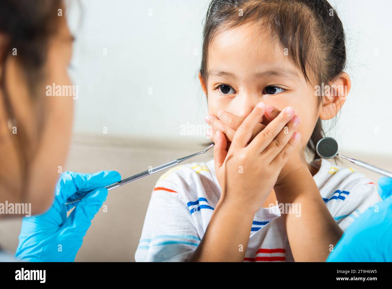 Piccolo capretto spaventato e chiude la bocca con le mani medico esamina la cavità orale Foto Stock