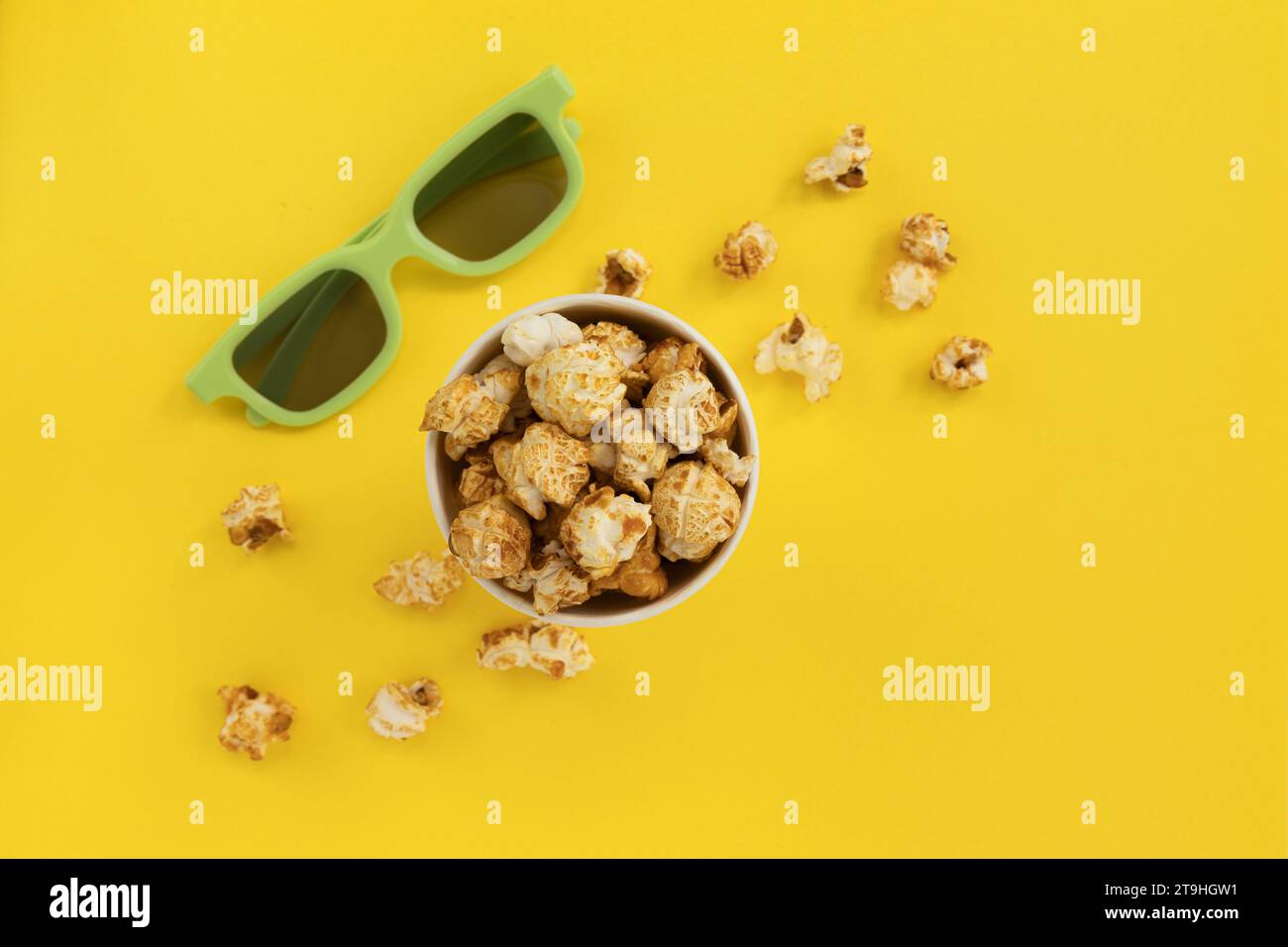 Popcorn caramello in secchiello di carta e occhiali 3D su sfondo giallo, Home Cinema, vista dall'alto Foto Stock
