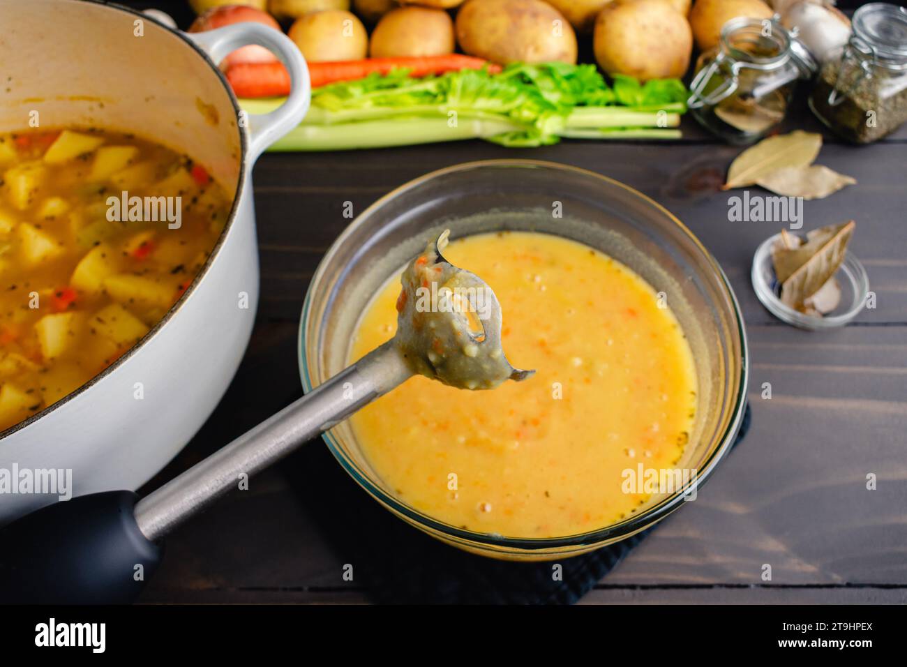 Primo piano di un frullatore a immersione con zuppa di patate sullo sfondo: Frullatore a bastone utilizzato per miscelare la zuppa di patate tedesca (kartoffelsuppe) in un recipiente di vetro Foto Stock