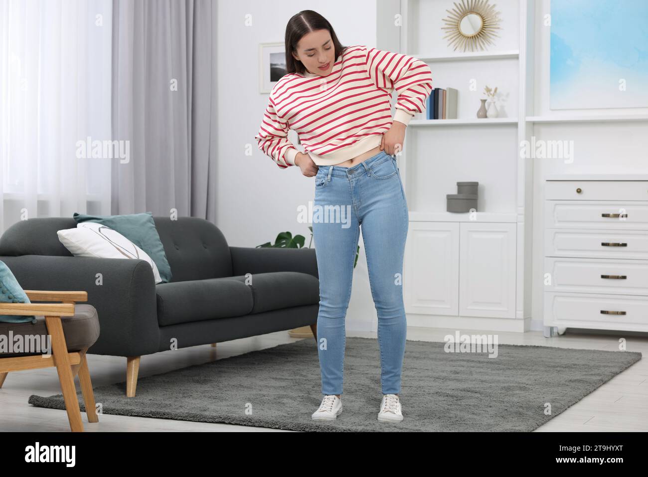 Donna che cerca di indossare jeans stretti a casa Foto Stock