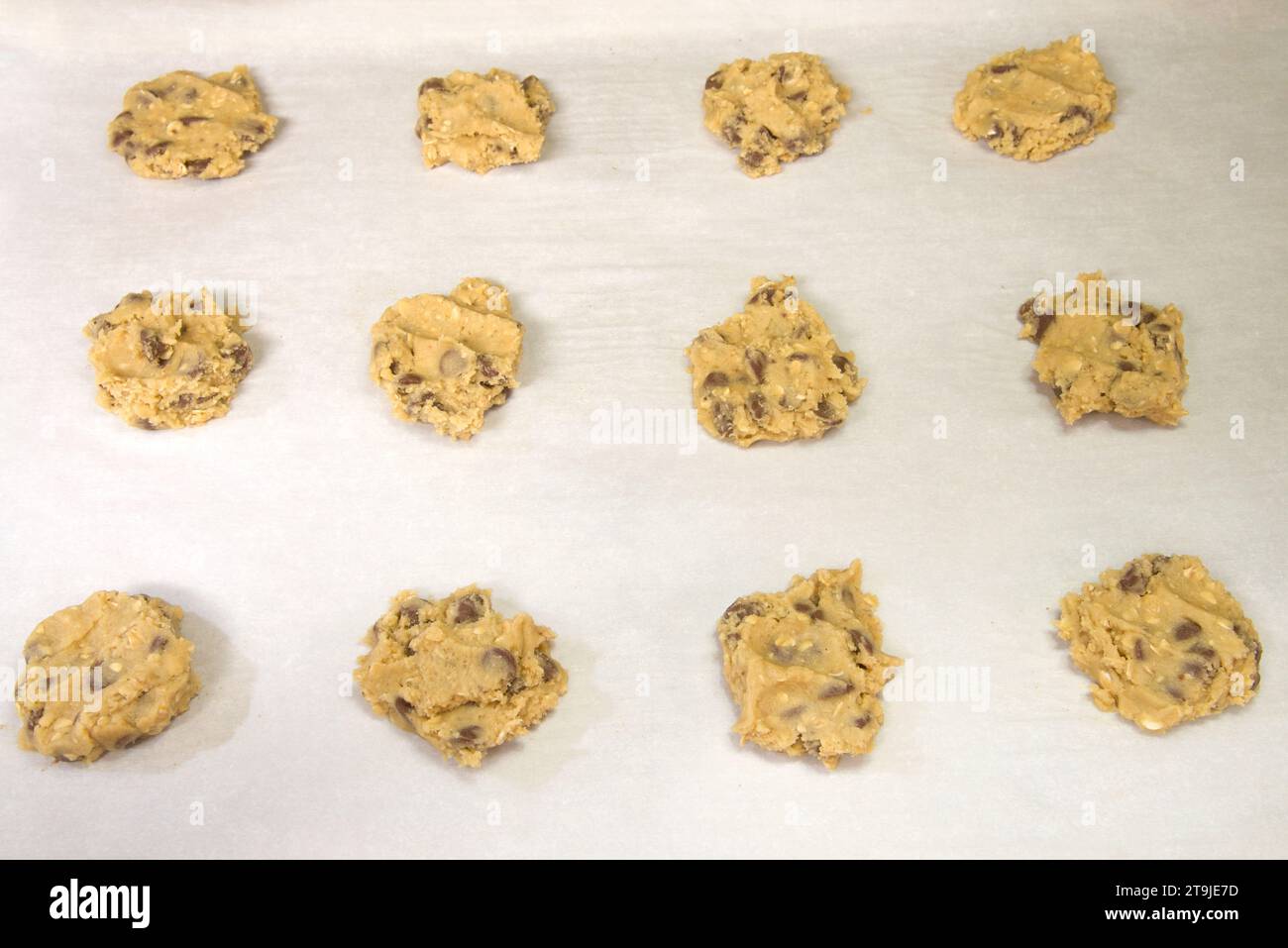 File di pasta fresca con scaglie di cioccolato e farinata d'avena, cucchiai su carta pergamena, pronta per la cottura. Foto Stock