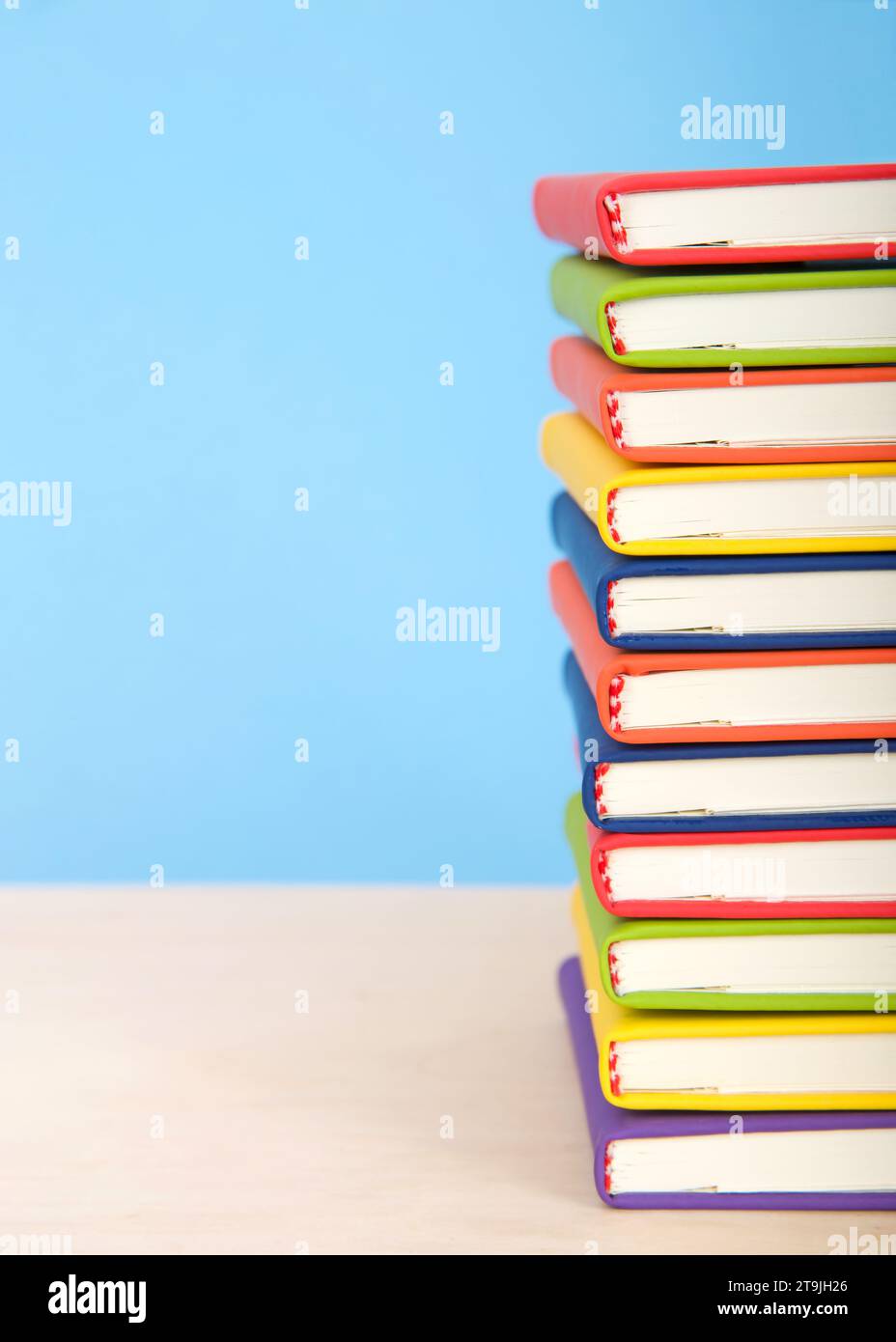 Primo piano su libri rilegati colorati e luminosi impilati su un tavolo di legno chiaro con sfondo blu. Metà dei libri in mostra. Minimalismo. Foto Stock