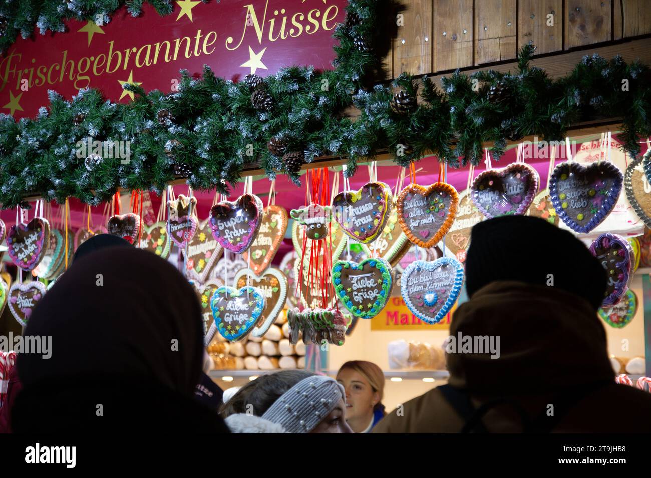 Outlet di vendita ambulante che vende torta al cioccolato a forma di cuore e visitatori affollati al mercatino di Natale (Wiener Christkindlmarkt) di sera in inverno Foto Stock