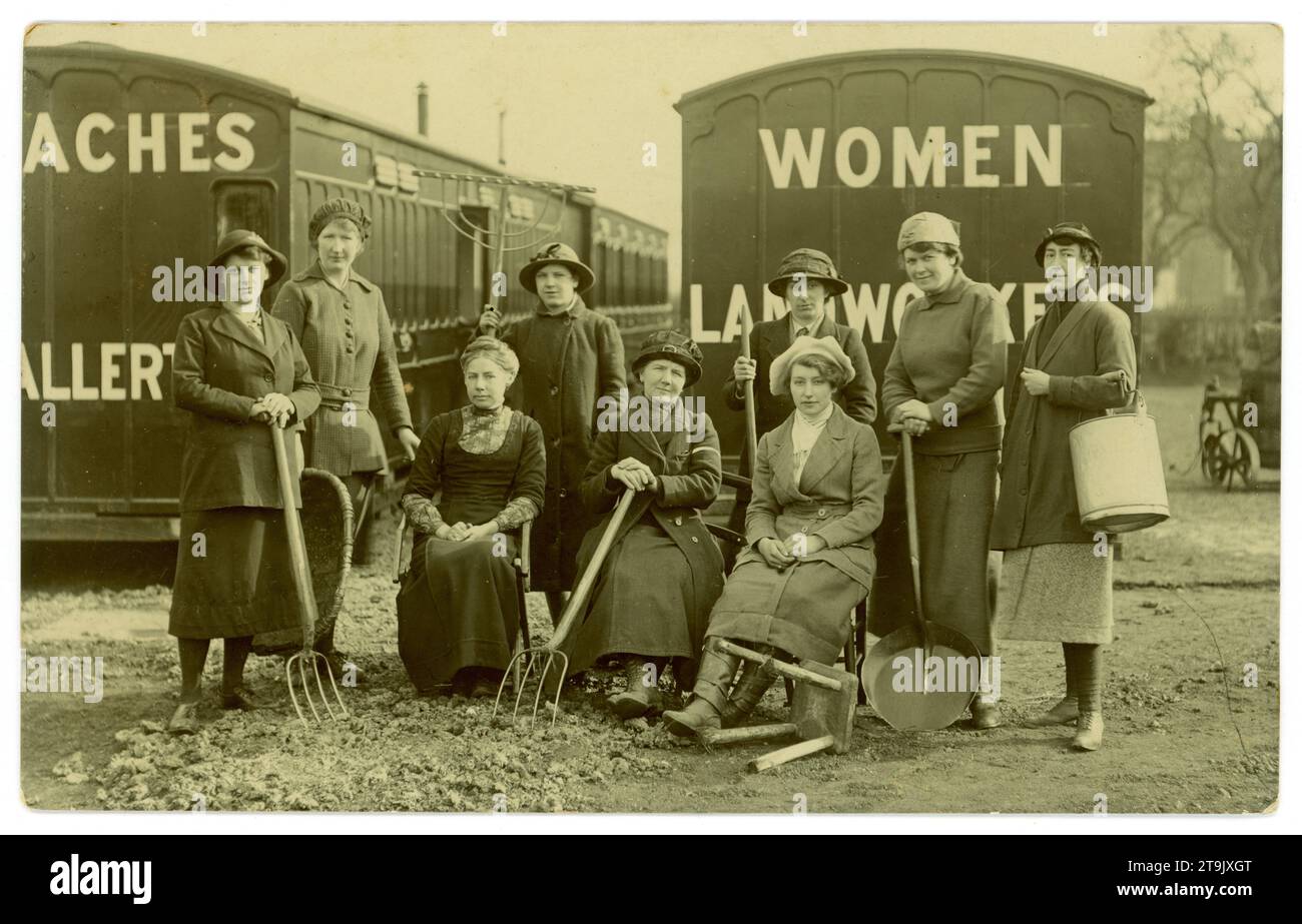 Cartolina originale dell'era della prima guerra mondiale di donne che reclutano lavoratori terrestri/carrozze ferroviarie per le sistemazioni, Northallerton e lavoratori del terreno scritta su pullman. La donna in abiti civili davanti, che indossa un vestito, è probabilmente un organizzatore di reclutamento, un ufficiale o un allenatore. Si pensa che si tratti di una fotografia pubblicitaria per il reclutamento, in quanto le donne sono in possesso di una selezione di strumenti come forche, rastrello, una falda e lattina di latte e sgabello per mungere. Forse le donne sono state in un corso di addestramento militare terrestre. Al contrario è scritto "1st set of landworkers Feb 26th to March 26th 1917" Northallerton, North Yorkshire, Regno Unito Foto Stock