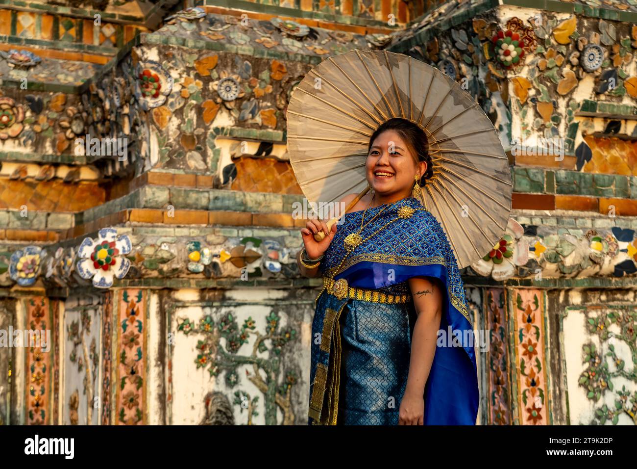 Festlich traditionell gekleidete Frau mit Schirm posiert vor dem Tempel Wat Arun oder Tempel der Morgenröte a Bangkok, Thailandia, Asien | Traditio Foto Stock