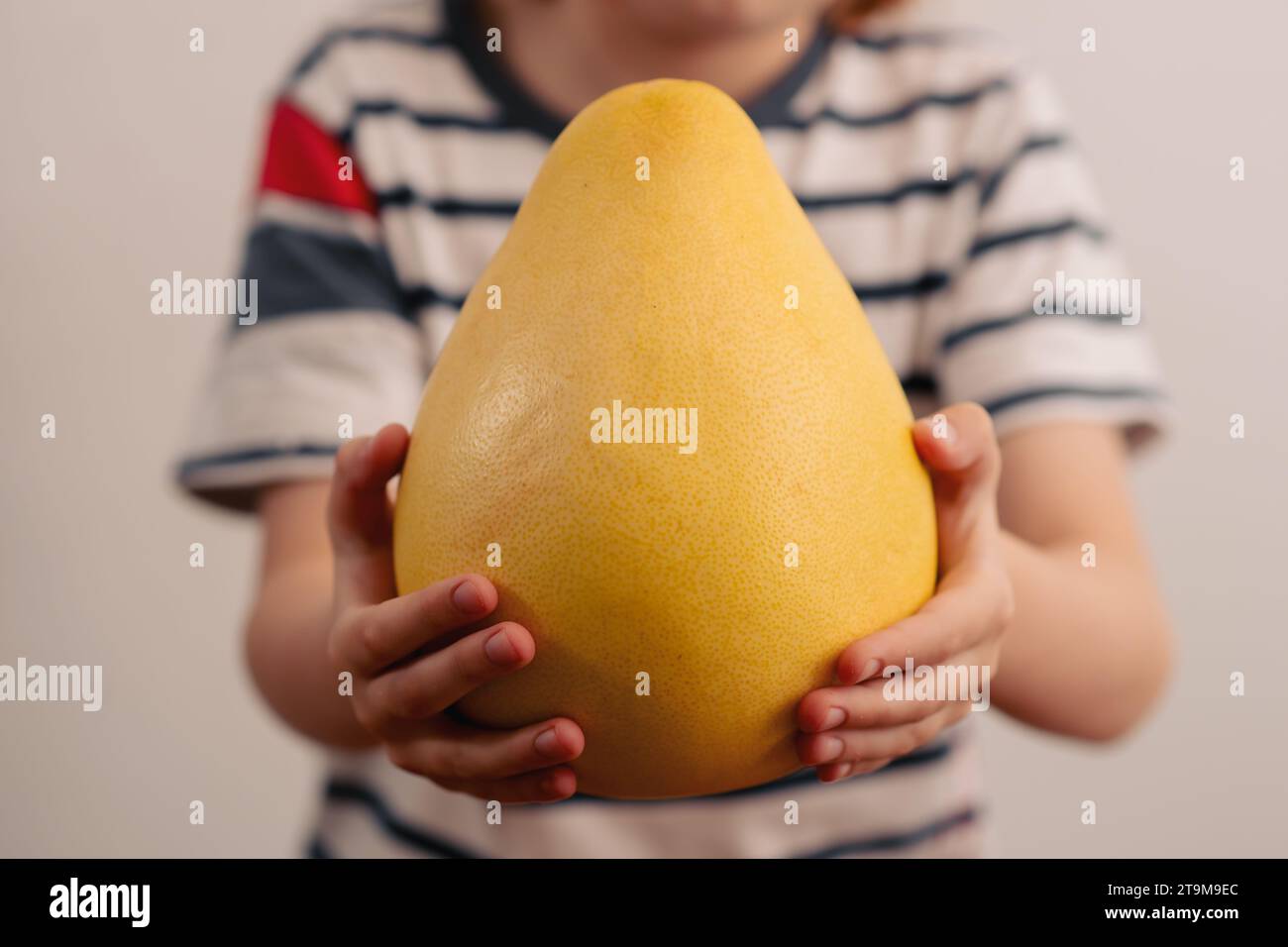 Delizia ricca di nutrienti: Un bambino esplora le meraviglie di un pomelo giallo considerevole, promuovendo i benefici per la salute derivanti dall'incorporazione della frutta nella vita quotidiana Foto Stock