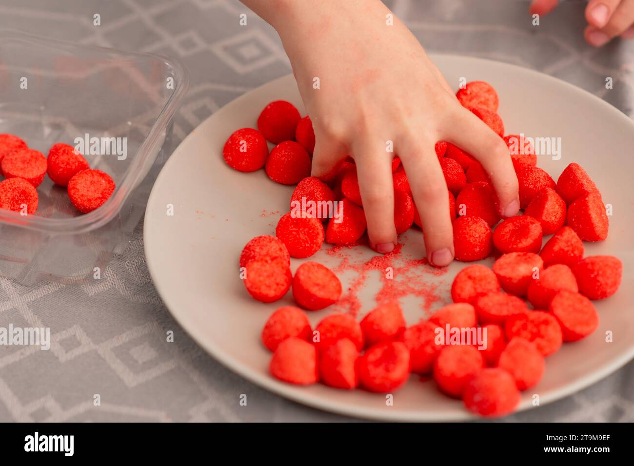 Delizia per i bambini: Le piccole dita afferrano le caramelle rosse fruttate, un'adorabile rappresentazione dell'amore per i dolci Foto Stock