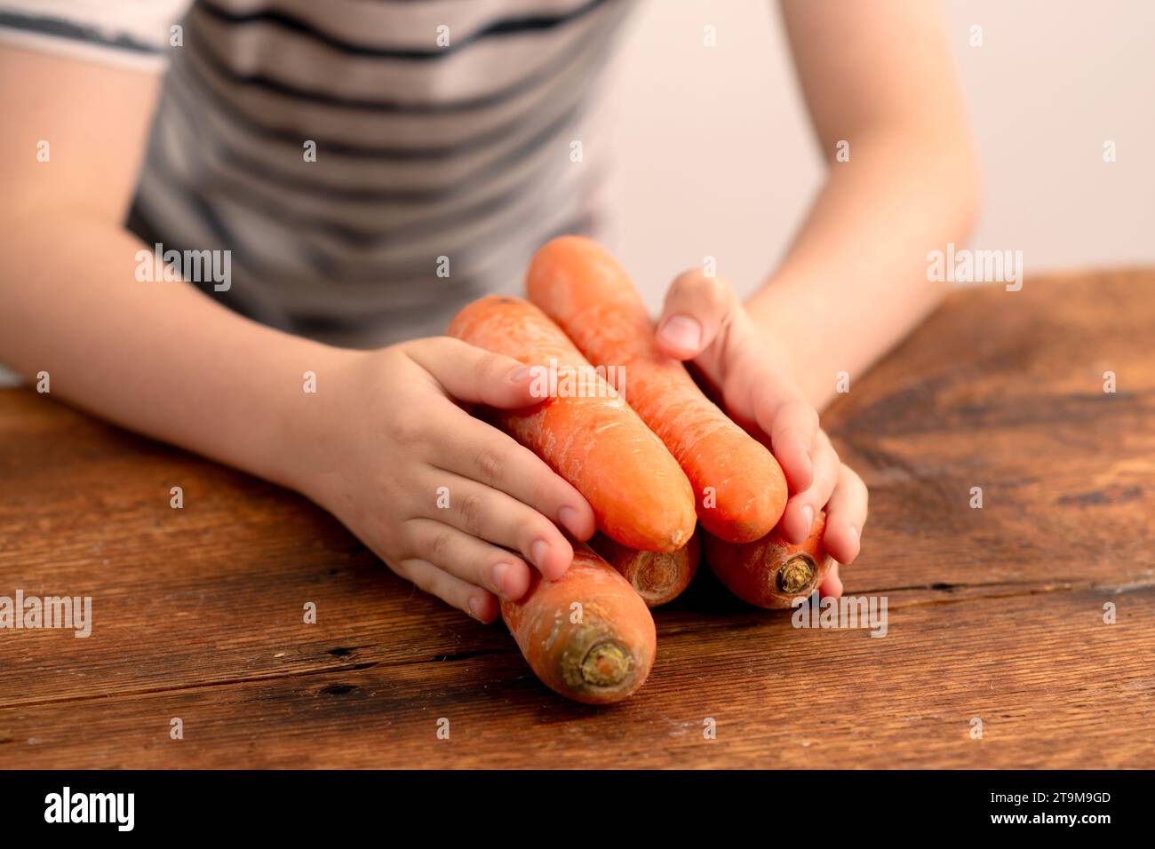 Le mani dei bambini reggono un mazzo di carote fresche, una vivace dimostrazione di raccolto sano su uno sfondo rustico di legno Foto Stock