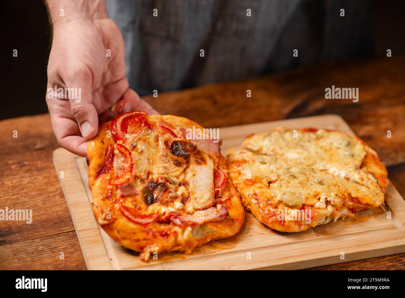 Pizza Perfection: Un uomo presenta con orgoglio una pizza fatta in casa su una superficie di legno, mostrando la sua creazione culinaria Foto Stock