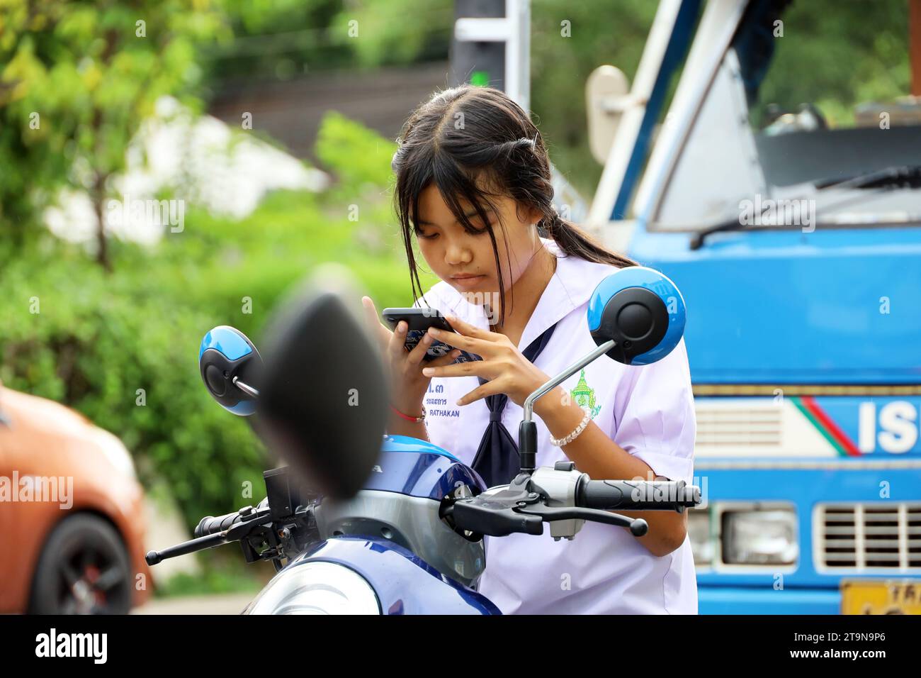 Ragazza thailandese che usa lo smartphone mentre si guida in moto per strada Foto Stock