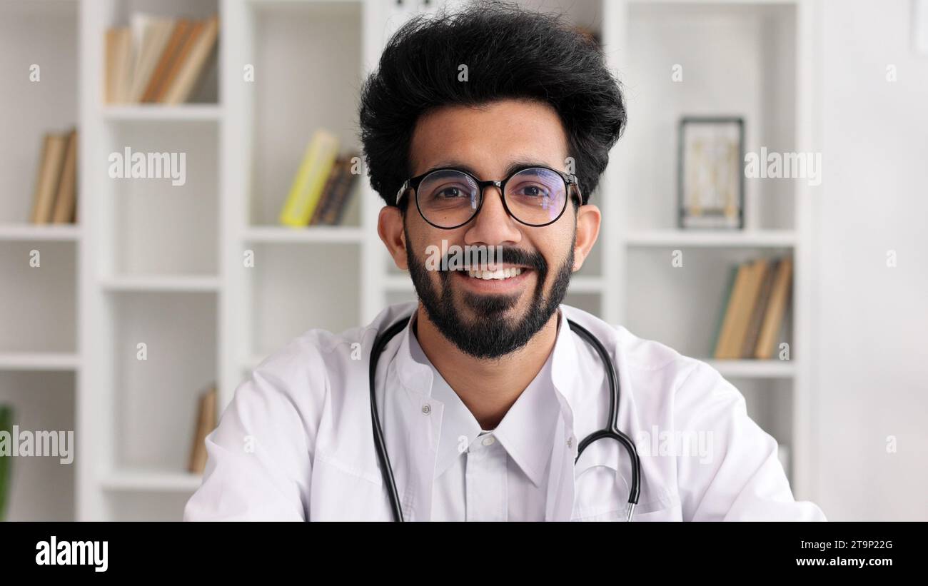 Ritratto di un giovane medico indiano che sorride e guarda la macchina fotografica in un cappotto bianco con uno stetoscopio. Vista ravvicinata. Foto Stock