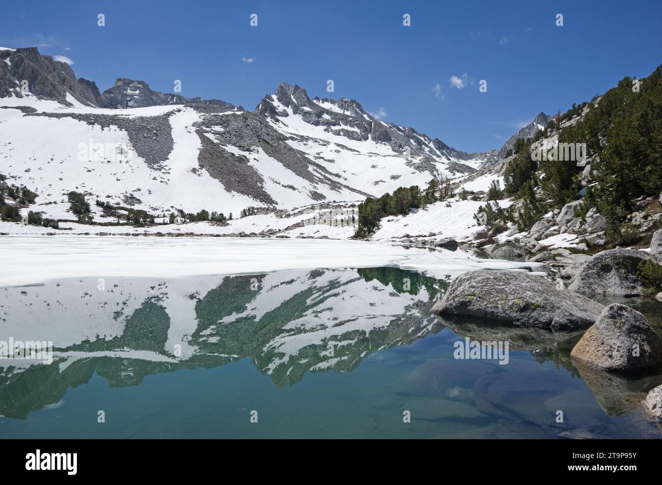 Echo Peak si riflette in un lago Moonlight parzialmente ghiacciato e innevato nel John Muir Wilderness a luglio Foto Stock