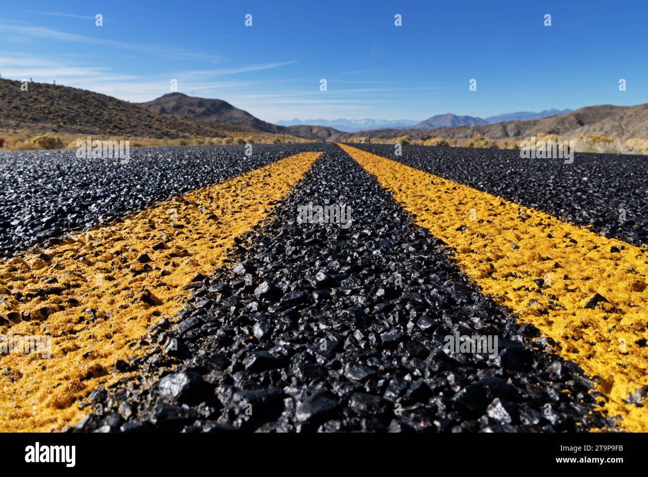 primo piano di una strada remota e di linee gialle che conducono verso montagne lontane Foto Stock