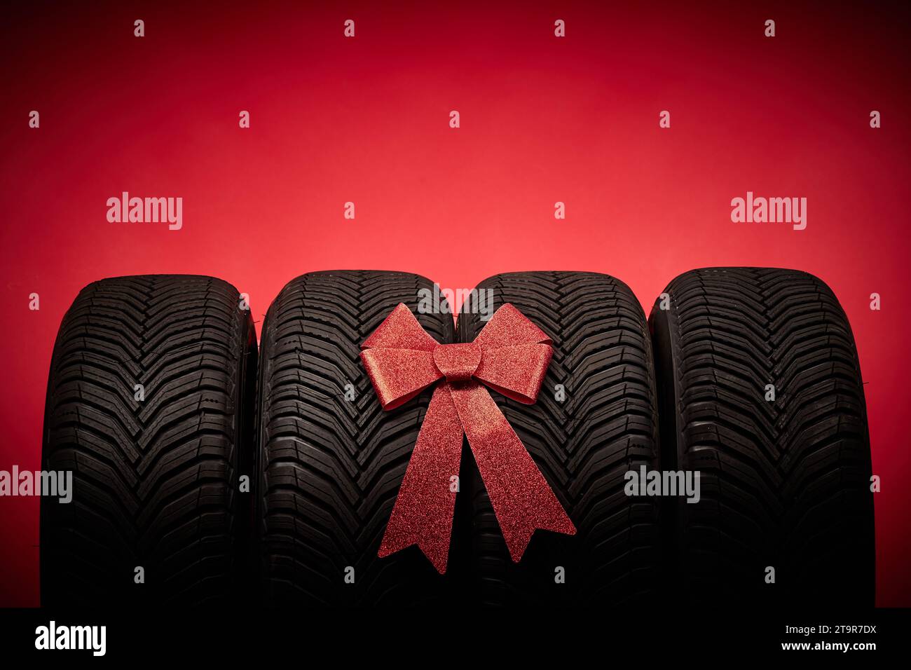 Pneumatici per auto, pneumatici nuovi, ruote invernali isolate su sfondo rosso natalizio con nastro di prua presente. Foto Stock