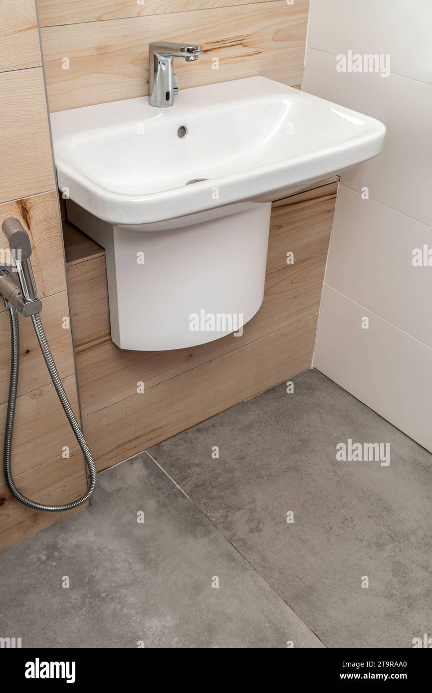 Lavello in porcellana bianca a parete con rubinetto in argento nel bagno moderno con piastrelle in cemento e legno Foto Stock