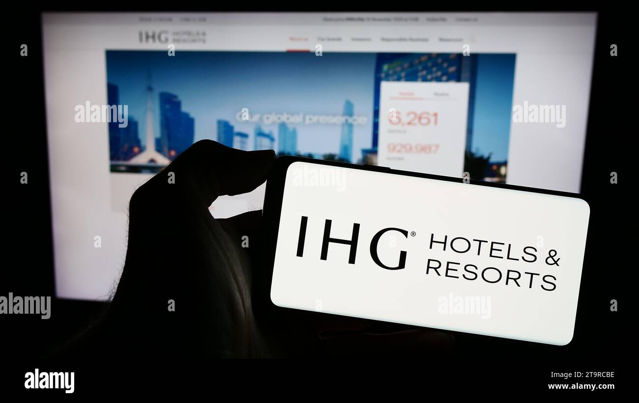 Persona che possiede uno smartphone con il logo della società alberghiera InterContinental Hotels Group plc (IHG) davanti al sito Web. Concentrarsi sul display del telefono. Foto Stock