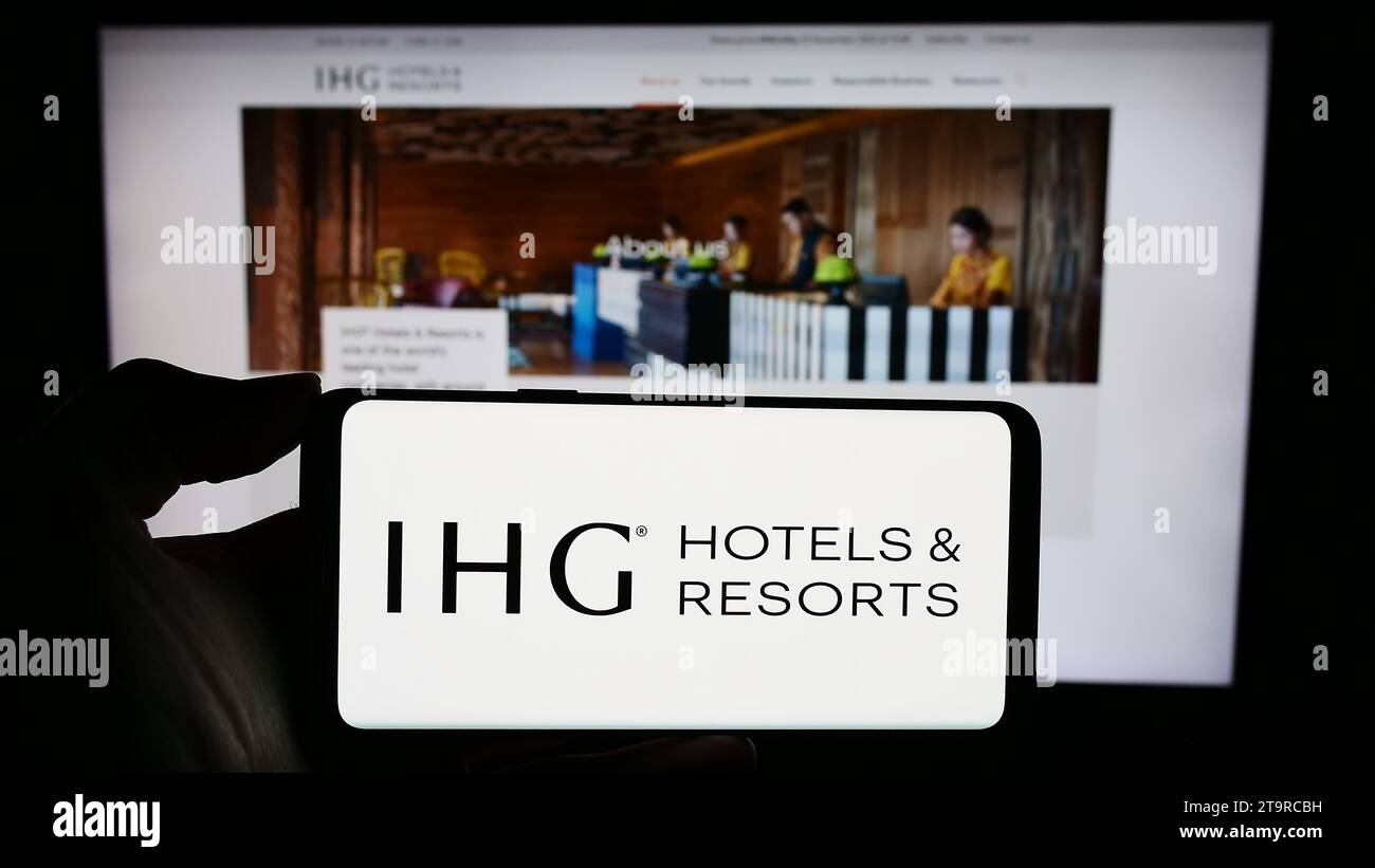Persona in possesso di un cellulare con il logo della società alberghiera InterContinental Hotels Group plc (IHG) davanti alla pagina Web aziendale. Concentrarsi sul display del telefono. Foto Stock