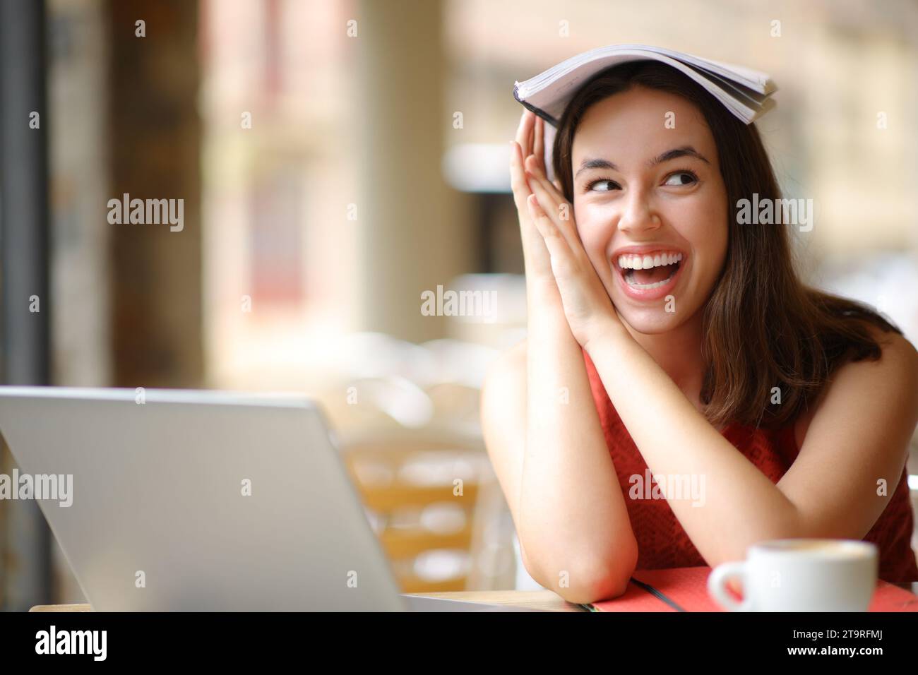 Allieva allegra che scherza con un notebook in testa che guarda di lato in un ristorante Foto Stock