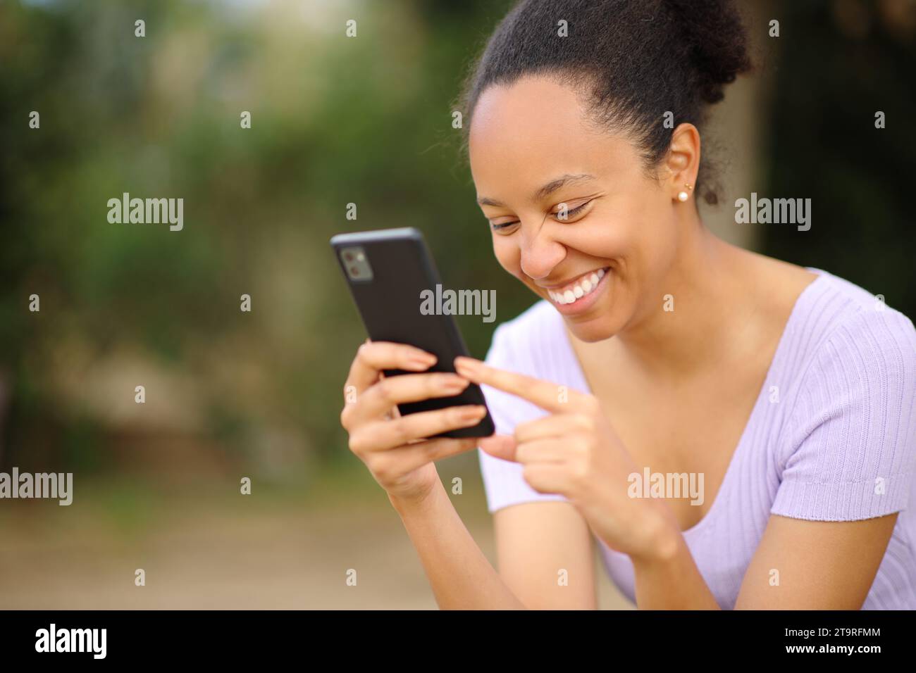 Felice donna nera che controlla le notizie sugli smartphone in un parco Foto Stock