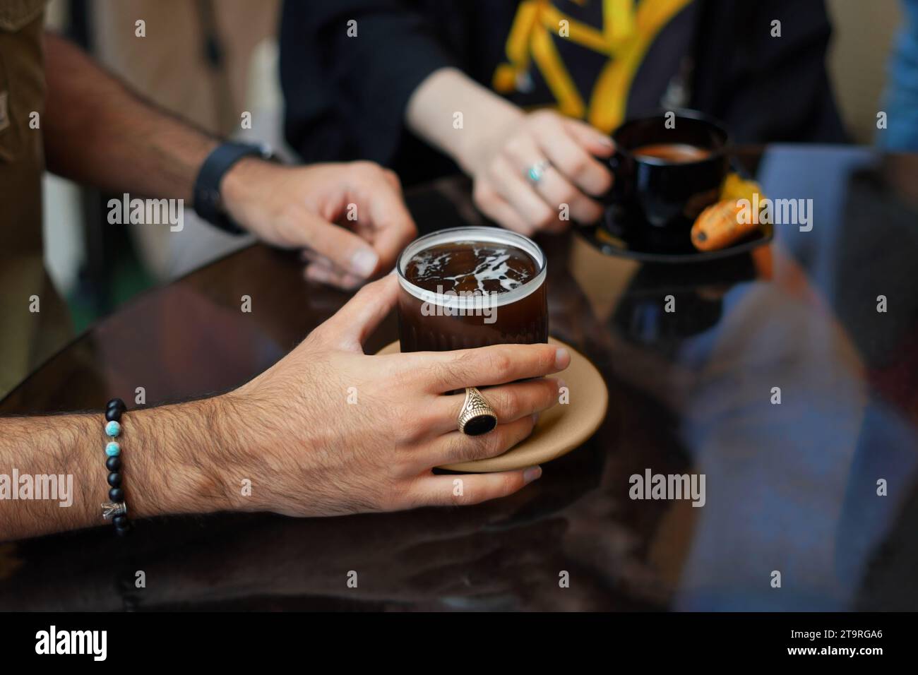 Primo piano delle mani maschili che tengono una tazza di caffè al tavolo e una mano femminile che tiene una tazza di caffè sullo sfondo. Foto Stock