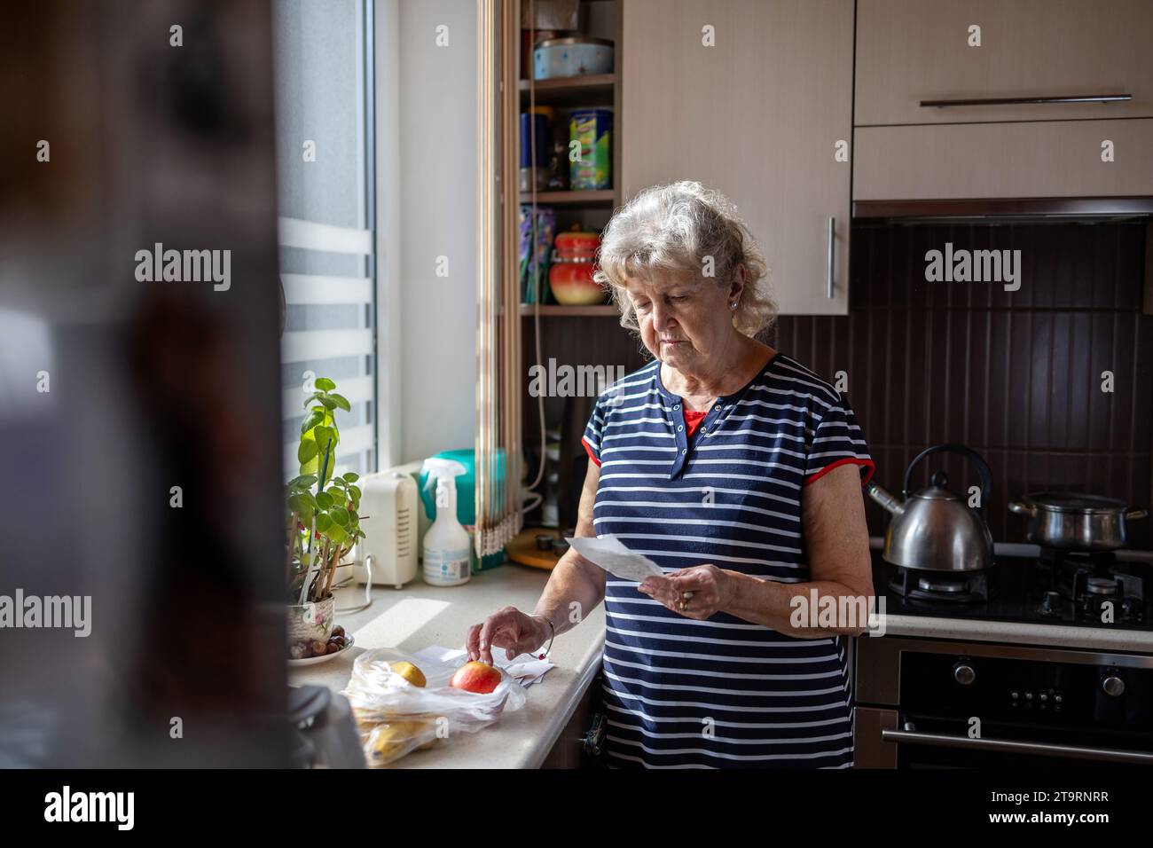 Donna anziana che passa attraverso le sue ricevute a casa dopo aver comprato generi alimentari Foto Stock