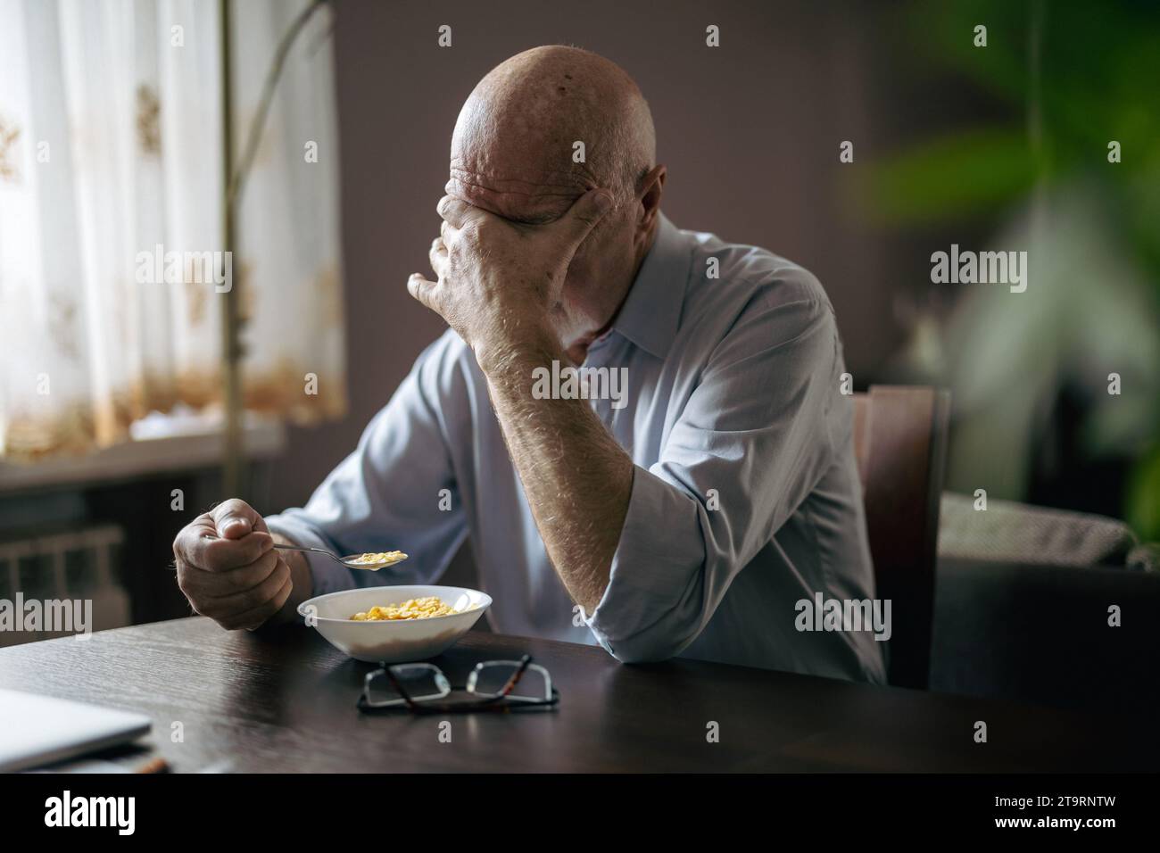 Un anziano depresso che fa colazione da solo a casa Foto Stock