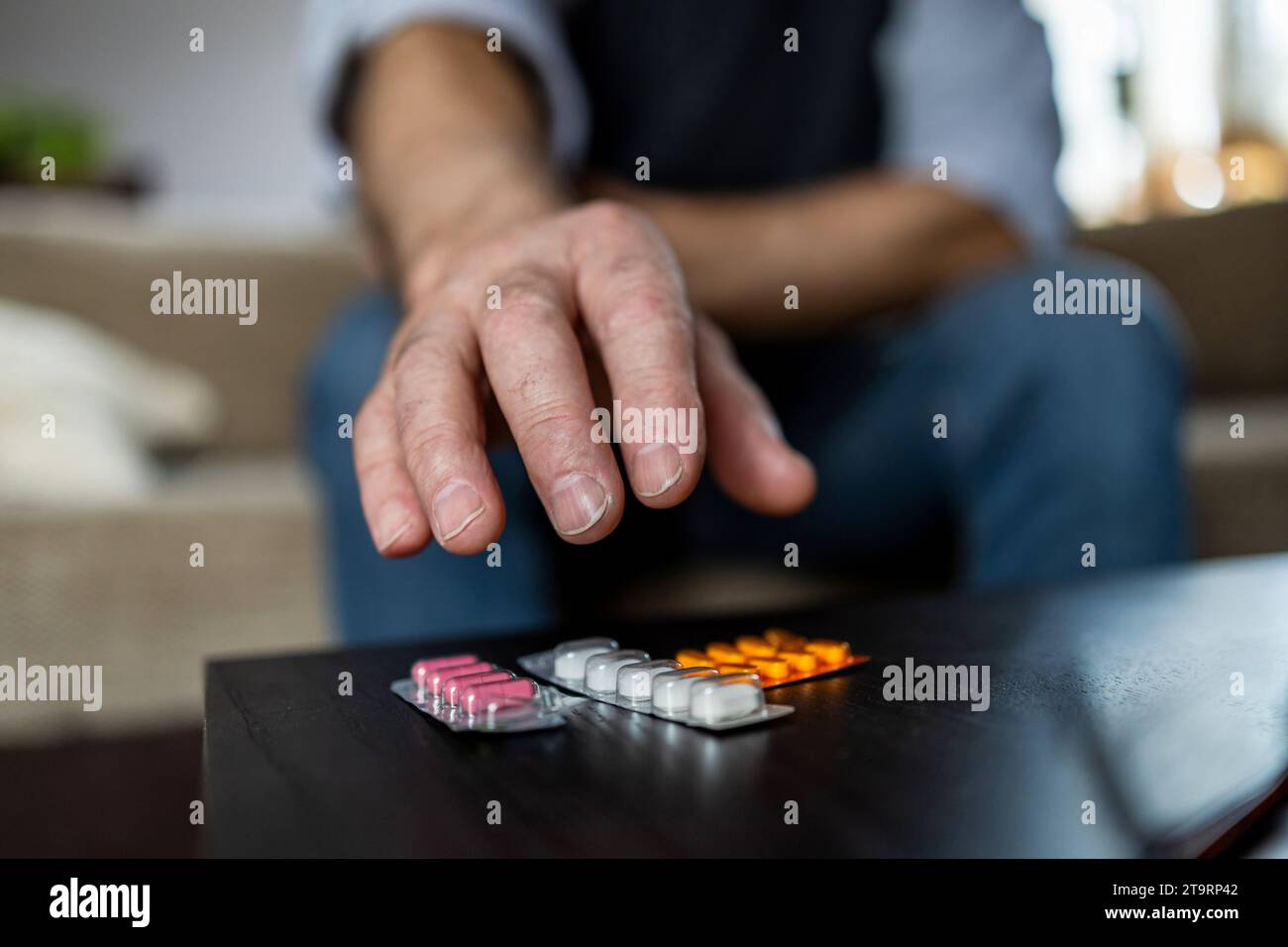 Primo piano di un uomo che prende pillole sul divano a casa nel soggiorno Foto Stock