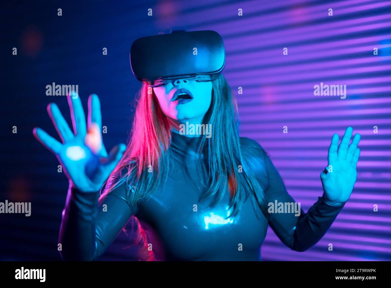 Donna sorpresa durante un gioco interattivo con occhiali VR in uno spazio notturno urbano con luci al neon Foto Stock