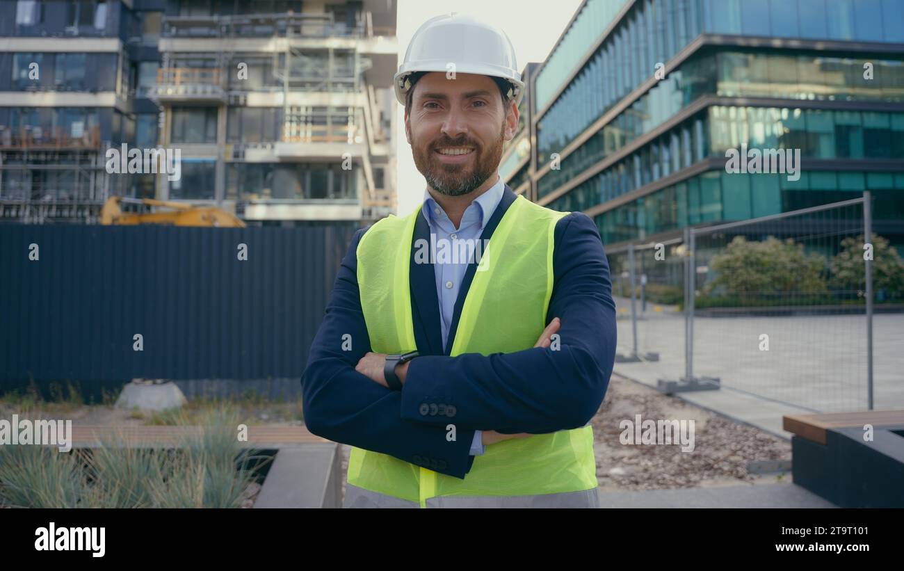 Sorridente uomo caucasico di mezza età lavoratore in hardhat felice sorriso ingegnere appaltatore in giubbotto da casco architetto ritrattista con le mani incrociate Foto Stock